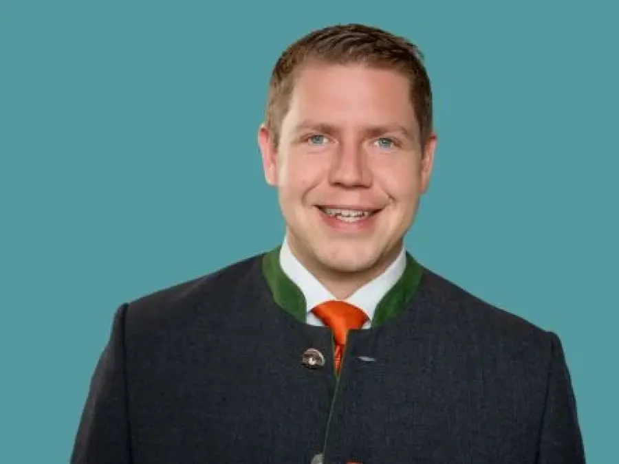 Portrait Daniel Schimmer, kurze blonde Haare, dunkelgrauer Janker mit Oranger Krawatte